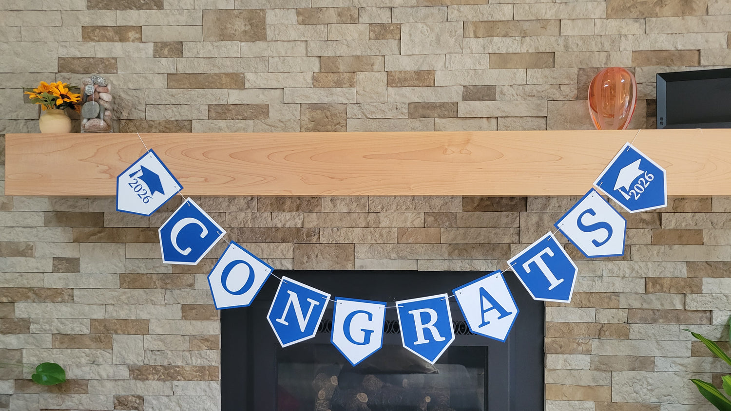 Graduation 'CONGRATS' banner on a fireplace with graduation cap and year design